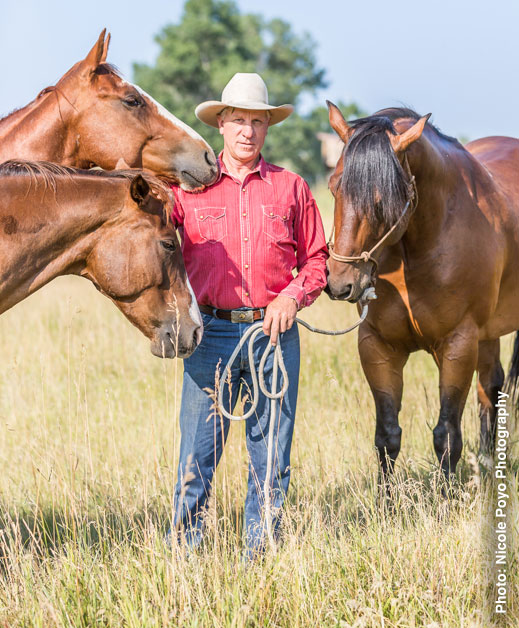 Buck in Red shirt and blue jeans posing with 3 horses in a field